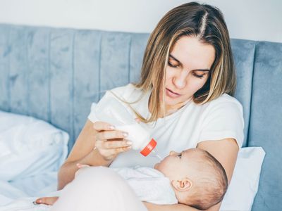 Mother feeding a newborn baby from bottle at home.