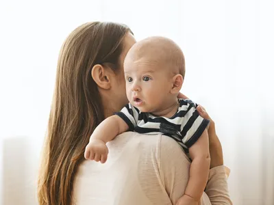 Mother patting adorable baby on back after breasfeeding