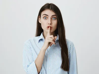 une jeune femme fait le signe du silence en plaçant son doigt sur sa bouche