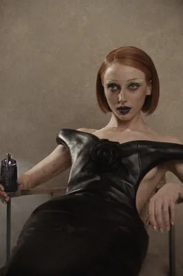 Portrait de créatrice rousse en robe de cuir noire tenant un flacon de parfum